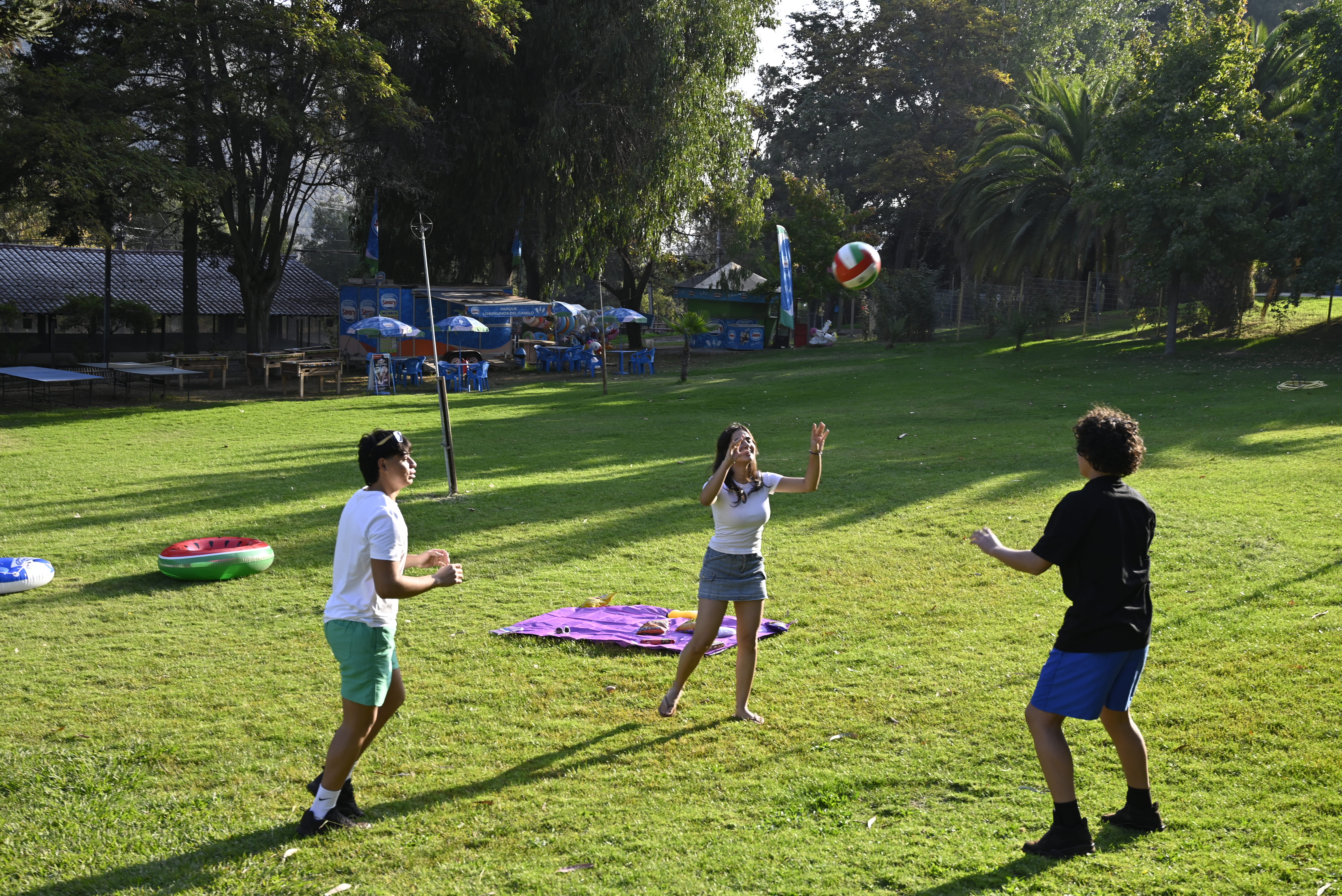 parque los peumos Niños y adolescentes jugando vóleibol en el pasto del Parque Los Peumos del Canelo, rodeados de árboles y zonas de picnic
